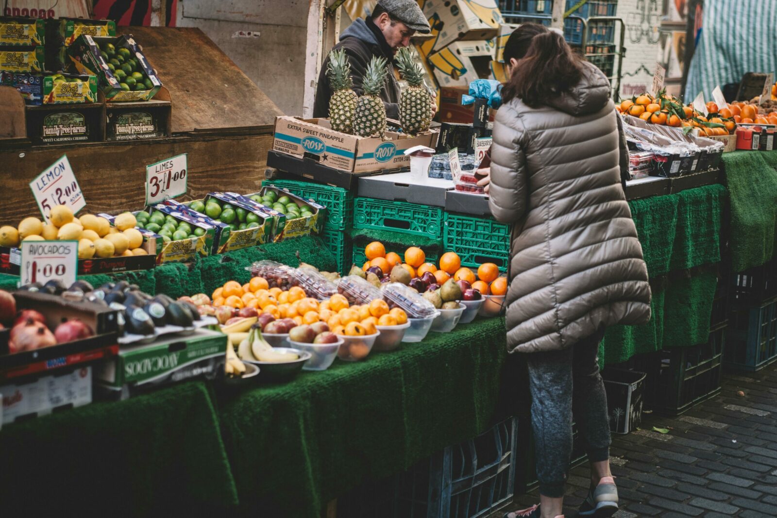 Lively city market stall displaying diverse fresh fruits. A customer browses.